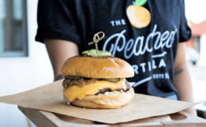 Server holding out a tray with a cheese burger and a pickle on top