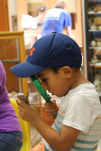 Little boy in blue cap looking through a magnifying glass at an object